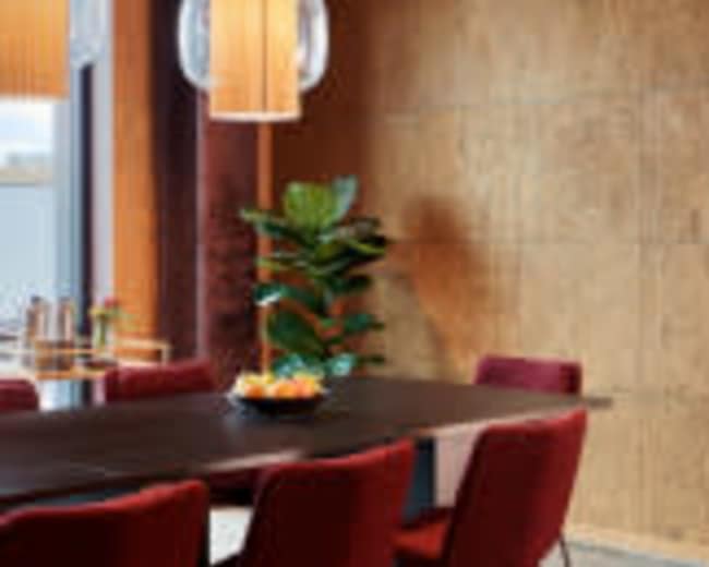 A dining area features a dark table surrounded by red chairs, with a plant and a pendant light illuminating the space.