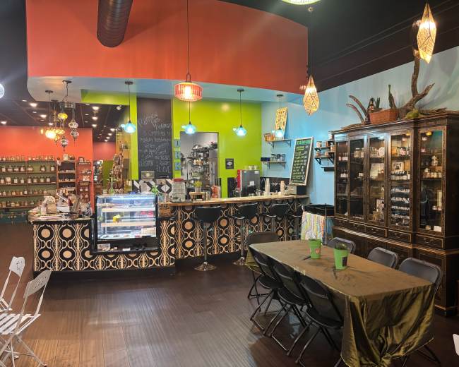 The image shows a colorful café interior with a service counter, showcasing desserts and a seating area with a table and chairs.