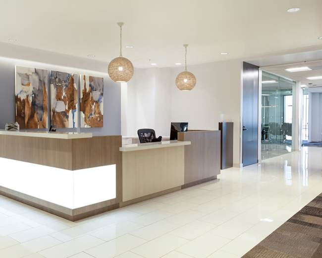 The image shows a modern reception area with a light-colored desk, decorative pendant lights, and abstract artwork on the wall.