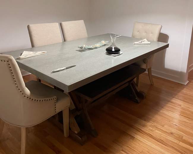 A minimalist dining area features a large gray table with four chairs and a pendant light hanging above.