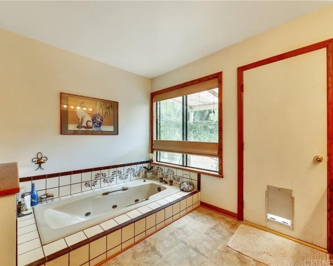 The image shows a bathroom featuring a jetted tub, tiled surfaces, a large window, and a door with a pet entry.