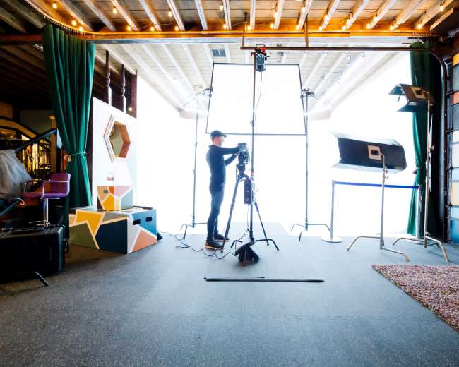 A photographer sets up equipment in a studio featuring large diffusion panels and colorful backdrops.