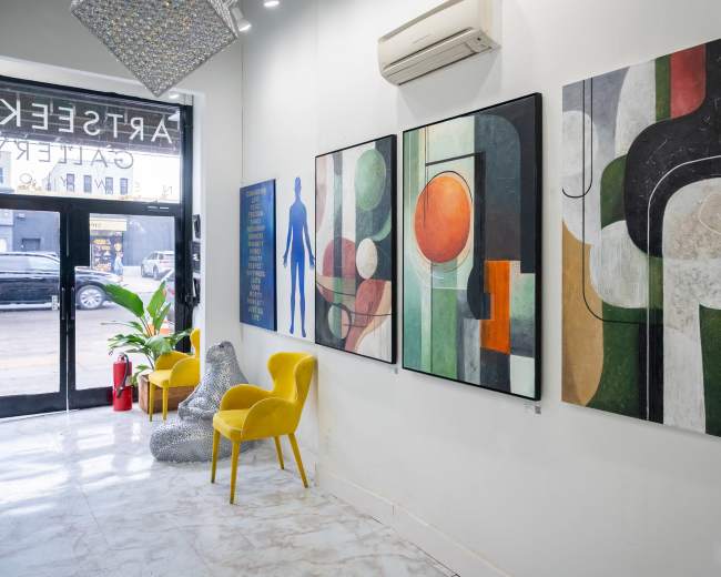 The image shows a modern art gallery featuring abstract paintings on the walls, colorful seating, and a large entrance window displaying a street view.