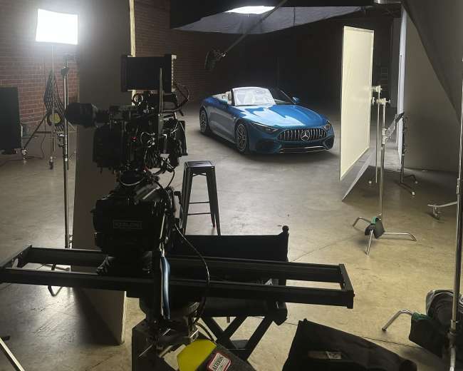 A camera setup is positioned in a studio, focusing on a blue sports car parked under studio lights.