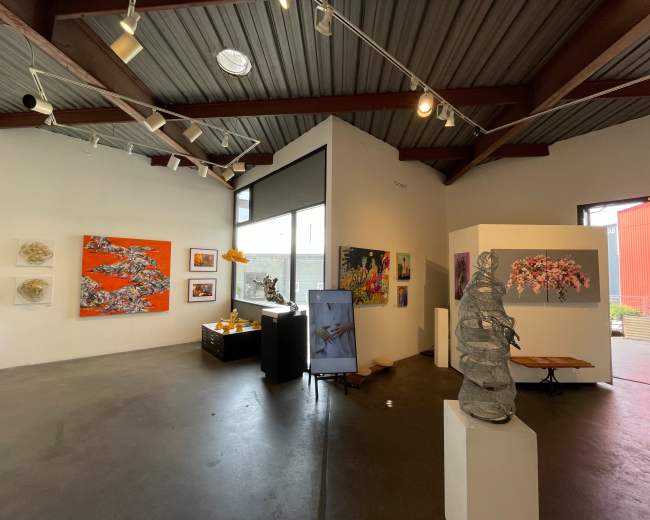 A modern art gallery featuring various colorful artworks on the walls, a sculpture in the center, and a display of objects on a table.