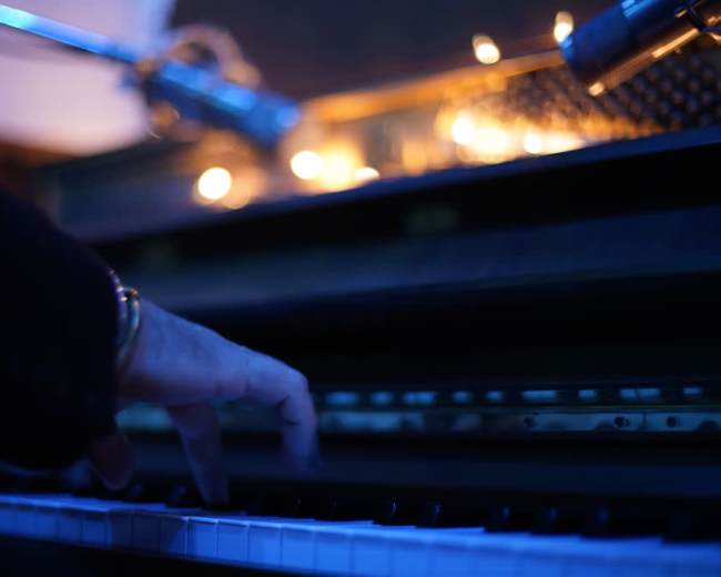 A hand plays the keys of a piano illuminated by soft, warm lights.
