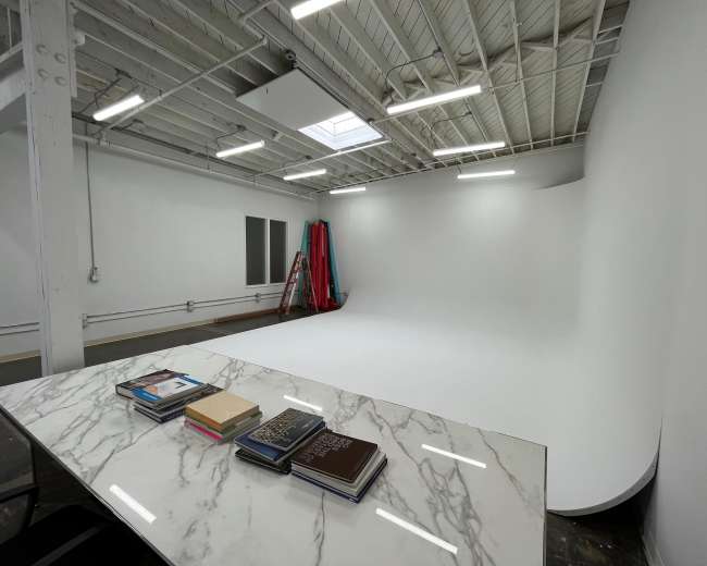 The image shows a spacious, well-lit studio with a curved white backdrop and a marble table displaying several stacked books.
