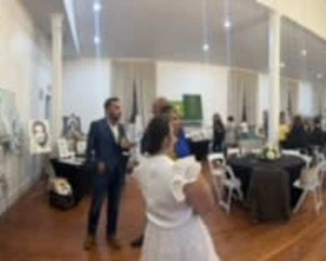 A large indoor space filled with people socializing at tables, with artwork displayed on the walls.