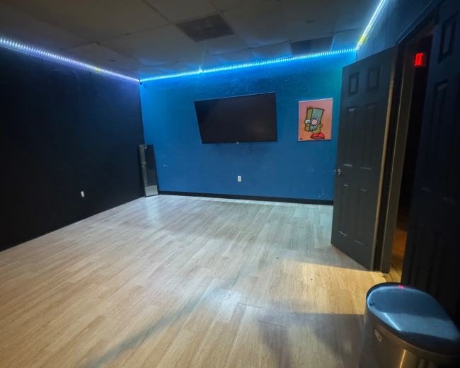 A sparsely furnished room features blue and black walls, a large television on the wall, and ambient lighting along the ceiling.