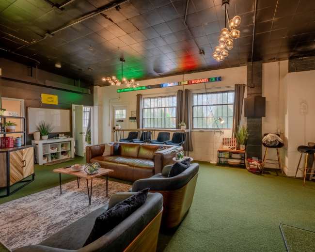 The image shows a spacious lounge area with modern furniture, green carpet, and decorative lighting.