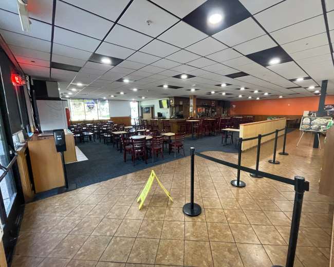 A largely empty restaurant interior with rows of chairs and tables, a cash register area, and caution signage on the floor.