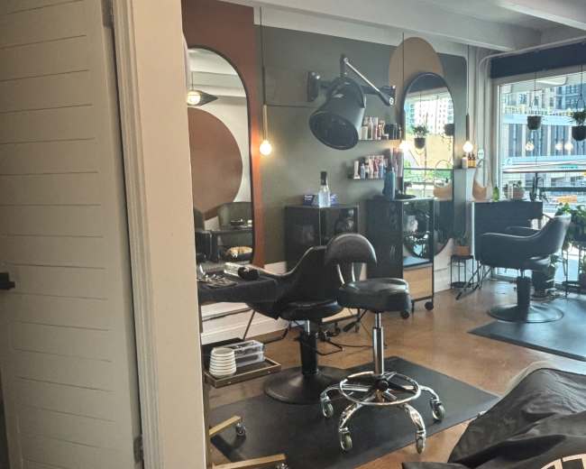 The image shows a modern hair salon interior with styling stations, mirrors, and a doorway leading to another area.