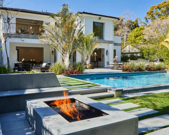 The image shows a modern two-story house with a spacious backyard featuring a pool, a fire pit, and landscaped greenery.