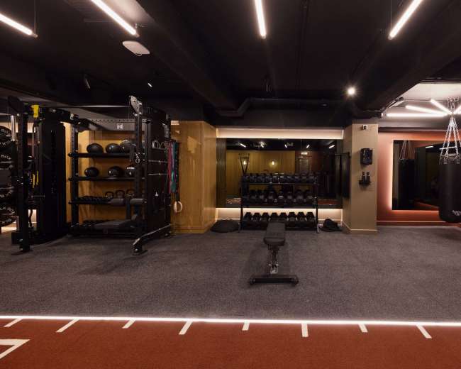 The image shows a modern gym interior equipped with various exercise machines, free weights, and a boxing bag, all set against a well-lit backdrop.