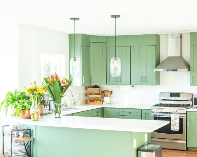 The kitchen features green cabinetry, a stainless steel stove, a white countertop, and a wooden island with plants and flowers.