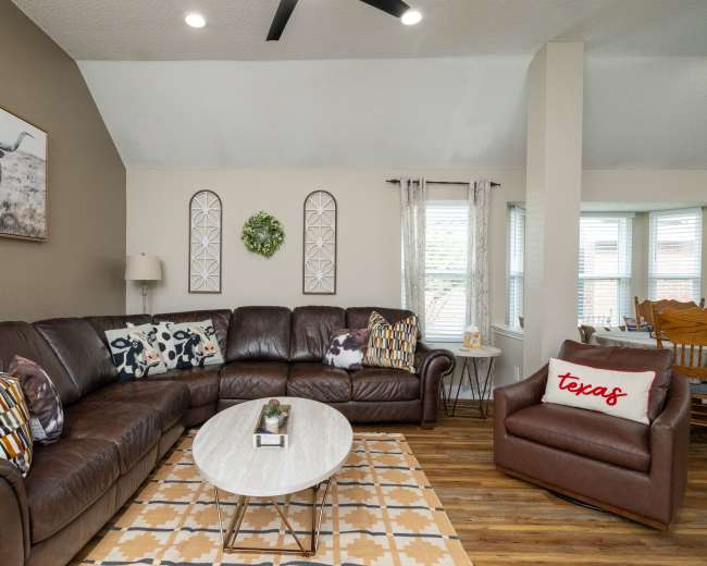 The living room features a brown leather sectional sofa, a round coffee table, and a rustic decor accent wall with a large framed picture of a longhorn steer.