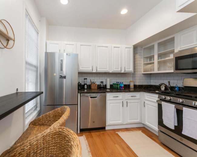 The kitchen features white cabinets, a stainless steel refrigerator, and a black countertop with a stove and dishwasher.