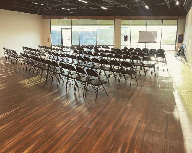 A spacious room with rows of empty chairs set up for an event, featuring large windows that allow natural light to fill the space.