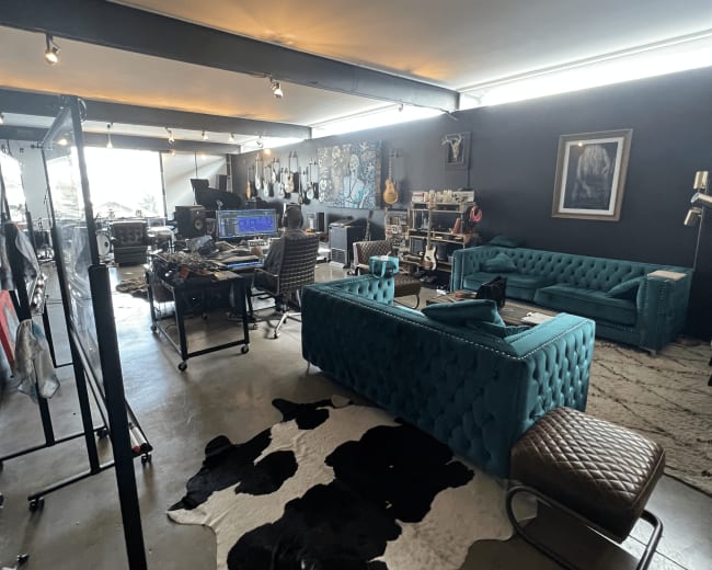 The image shows a spacious studio with turquoise tufted sofas, a cowhide rug on the floor, musical instruments on display, and various workstations set up for creative activities.