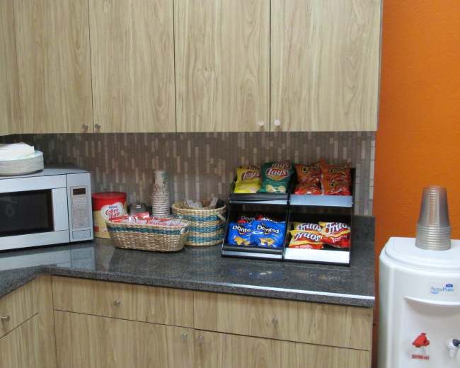 A kitchen countertop features a microwave, coffee maker, and a basket of snacks next to a mini fridge.
