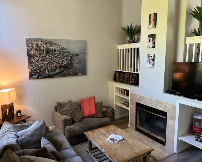 A cozy living room with a large cityscape painting, a comfortable sofa arrangement, a wooden coffee table, and a television set next to a fireplace.