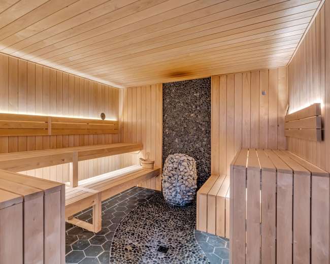 The image shows a wooden sauna with benches, a stone centerpiece, and illuminated wall features.