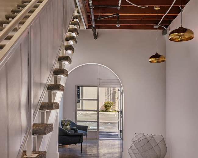 The image features a modern interior space with a staircase, an arched entryway, and pendant lighting, leading to a small seating area.