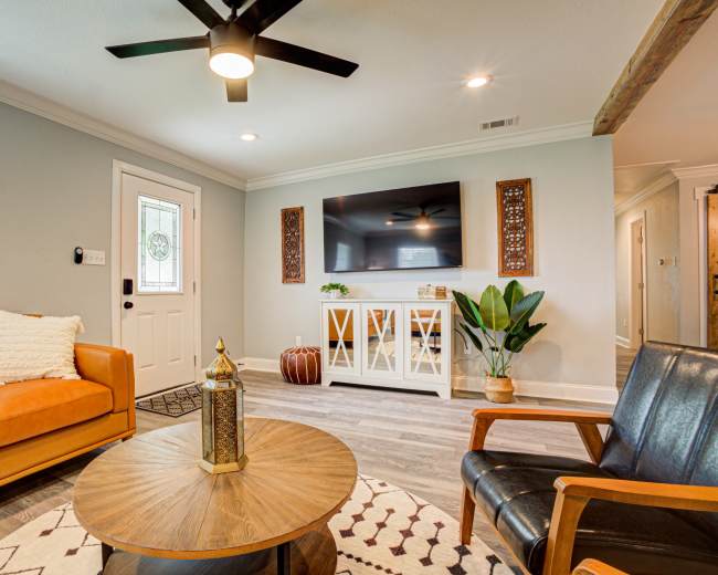 A modern living room featuring an orange leather sofa, a black armchair, a round wooden coffee table, a television mounted on the wall, and a potted plant.