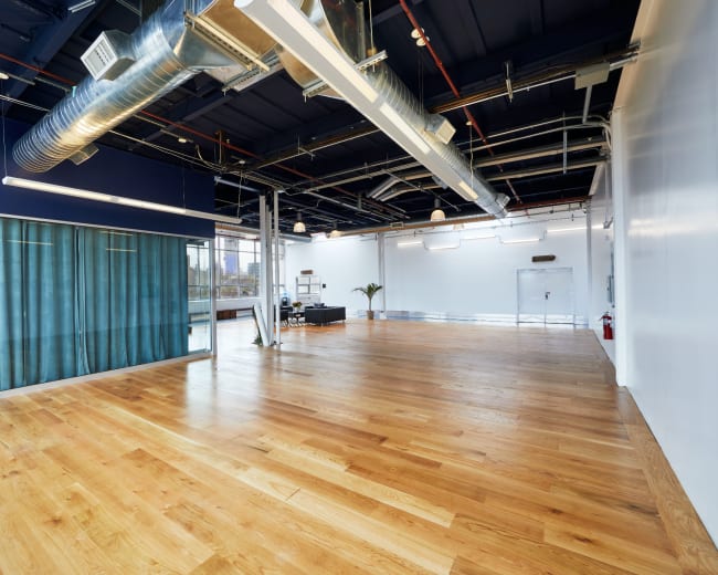 The image shows a spacious, modern interior with wooden flooring, large windows, and a blue wall with curtains.
