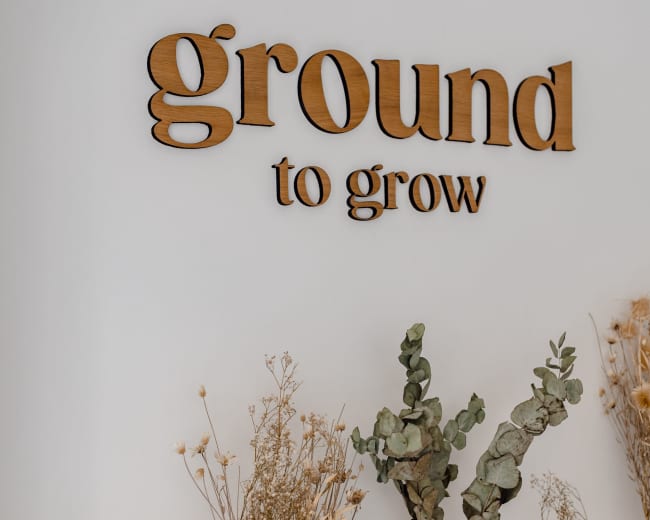 A white wall displays the phrase "ground to grow" in wooden letters above various decorative vases filled with dried plants.