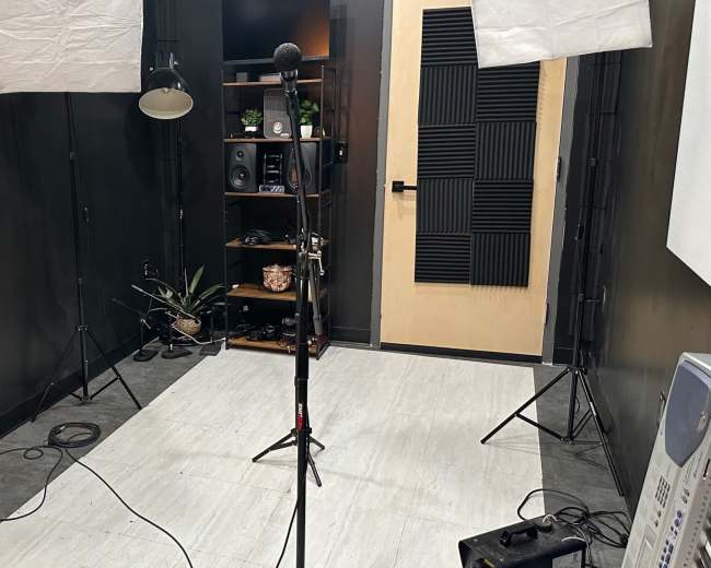 A music recording studio with a microphone stand, keyboard, and softbox lights set up against a dark wall.