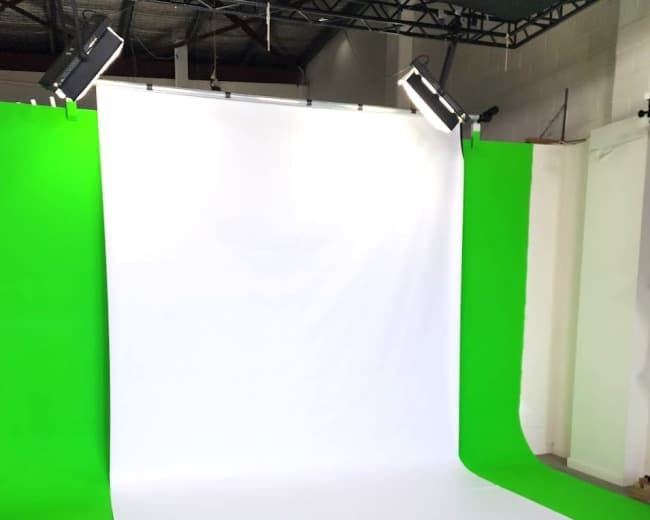The image shows a photography studio setup with a white backdrop and green side panels illuminated by overhead lights.