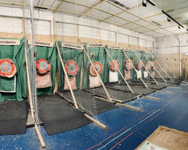 The image shows a series of target lanes for axe throwing, each with a segmented target mounted on a structure, all enclosed by nets.