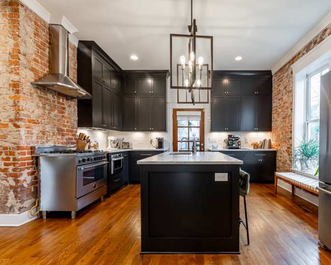 The kitchen features exposed brick walls, dark cabinetry, a marble island, and stainless steel appliances.