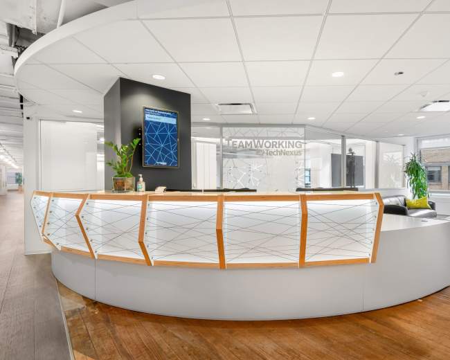 The image shows a modern reception area with a curved front desk, a digital display board, and large windows providing natural light.