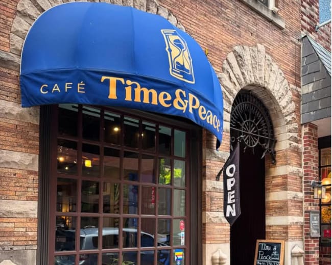 The image shows a café named "Time & Peace" with a blue awning, featuring outdoor seating with wooden tables and chairs in front of a large window.