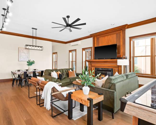 A spacious living room features a fireplace, dark wood accents, comfortable seating, and a dining area with a large table.