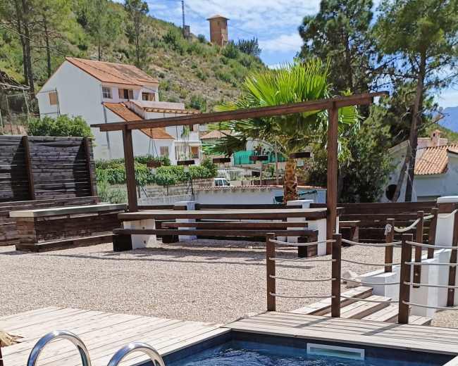 The image shows a wooden deck surrounding two swimming pools, with a landscaped area and buildings in the background.