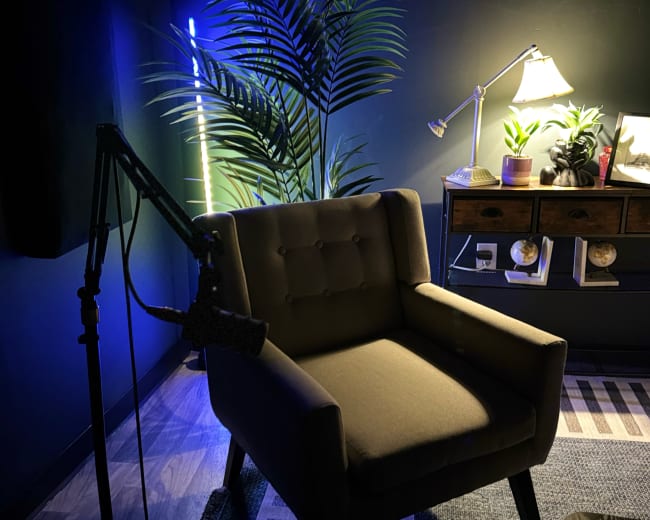 The image shows a cozy room featuring a brown armchair beside a desk with plants and a lamp, illuminated by soft blue lighting.