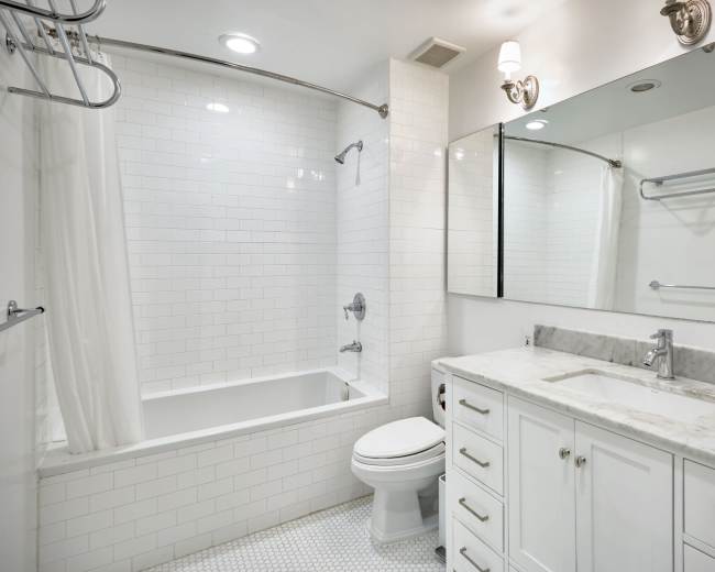 The image shows a modern bathroom featuring a white tiled shower, a bathtub, a wall-mounted mirror, and a vanity with a marble countertop.