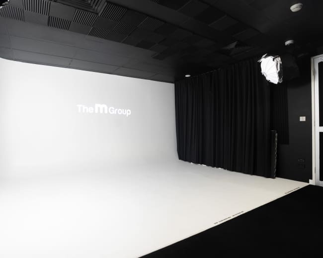 The image shows a spacious photography studio with a white backdrop and soft black curtains on one side.