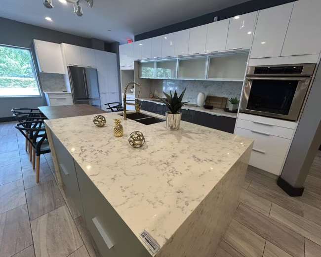 The image shows a modern kitchen featuring a marble island, sleek cabinetry, and stainless steel appliances.