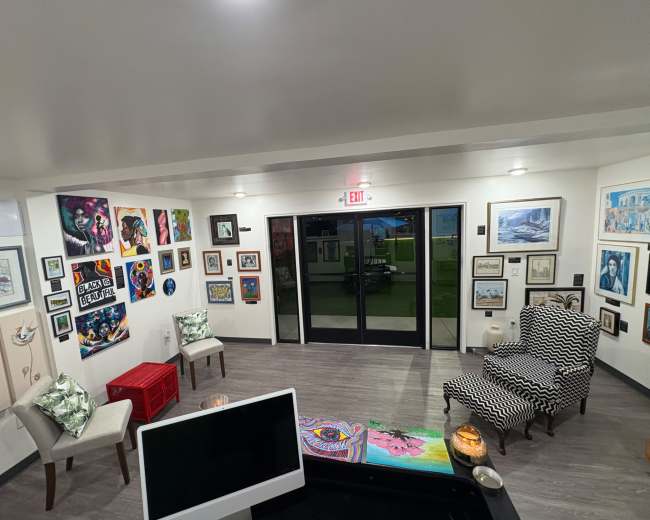 The image shows an interior room decorated with various pieces of artwork on the walls, a patterned armchair, and a visible exit door.