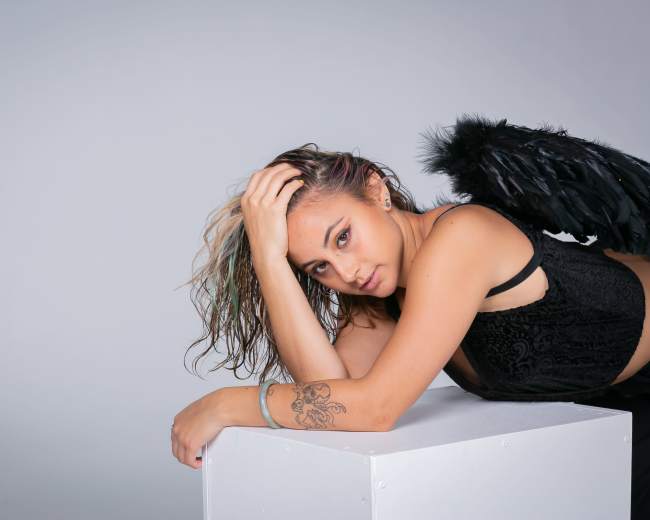 A person with wings lies on a white pedestal against a gray background.