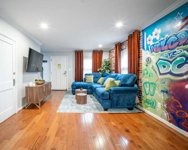 The living room features a blue sectional sofa, a wooden TV stand with a television, and a colorful graffiti mural on the wall.