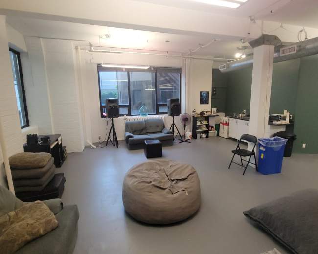The image shows a spacious room with a gray floor, several seating areas including bean bags and couches, and audio equipment set up near a window.