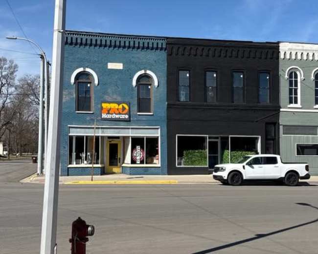 The image shows a street view of a two-story hardware store building with a blue facade and a large sign reading "PRO Hardware," located at a corner intersection.