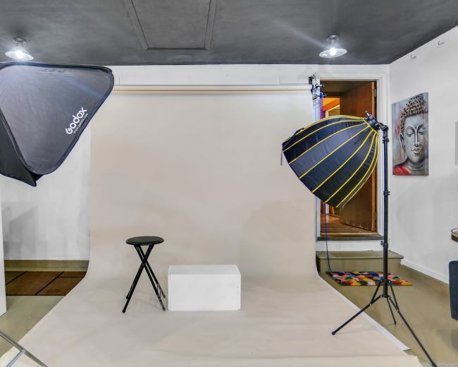 A photography studio setup featuring a plain backdrop, a stool, and two softboxes for lighting.