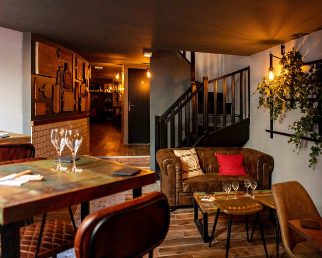 The image showcases a cozy interior of a restaurant featuring a staircase, tables, and a comfortable seating area with a brown couch and decorative plants.