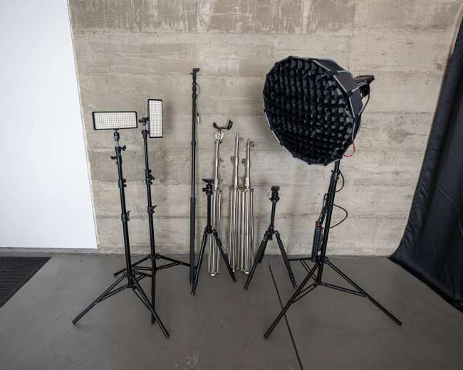 Various lighting equipment and stands arranged on a concrete floor next to a wall.